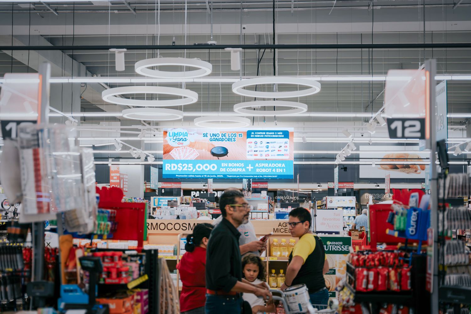 Compradores en Hipermercados Olé con pantalla LED al fondo
